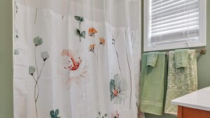 A bathroom with a floral shower curtain, a window with blinds, and two towels on a rack. - Cozy Bloomington Townhouse Close to IU Campus (Bloomington)