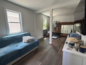 A room with a blue sofa, a wooden floor, a large mirror, and a white cabinet with decorative items.