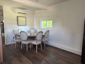 Un comedor con una mesa y sillas, un equipo de aire acondicionado, una ventana y un cuadro en la pared.