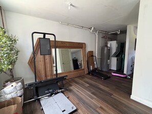Una habitación con un espejo de marco de madera, un piano, una caminadora y una planta grande en maceta.