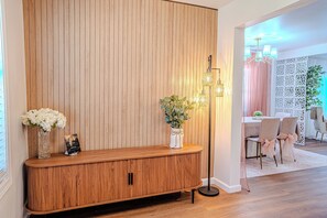Ein hölzerner Empfangstresen mit Blumen, eine Stehlampe und ein Essbereich mit Stühlen und Tisch.