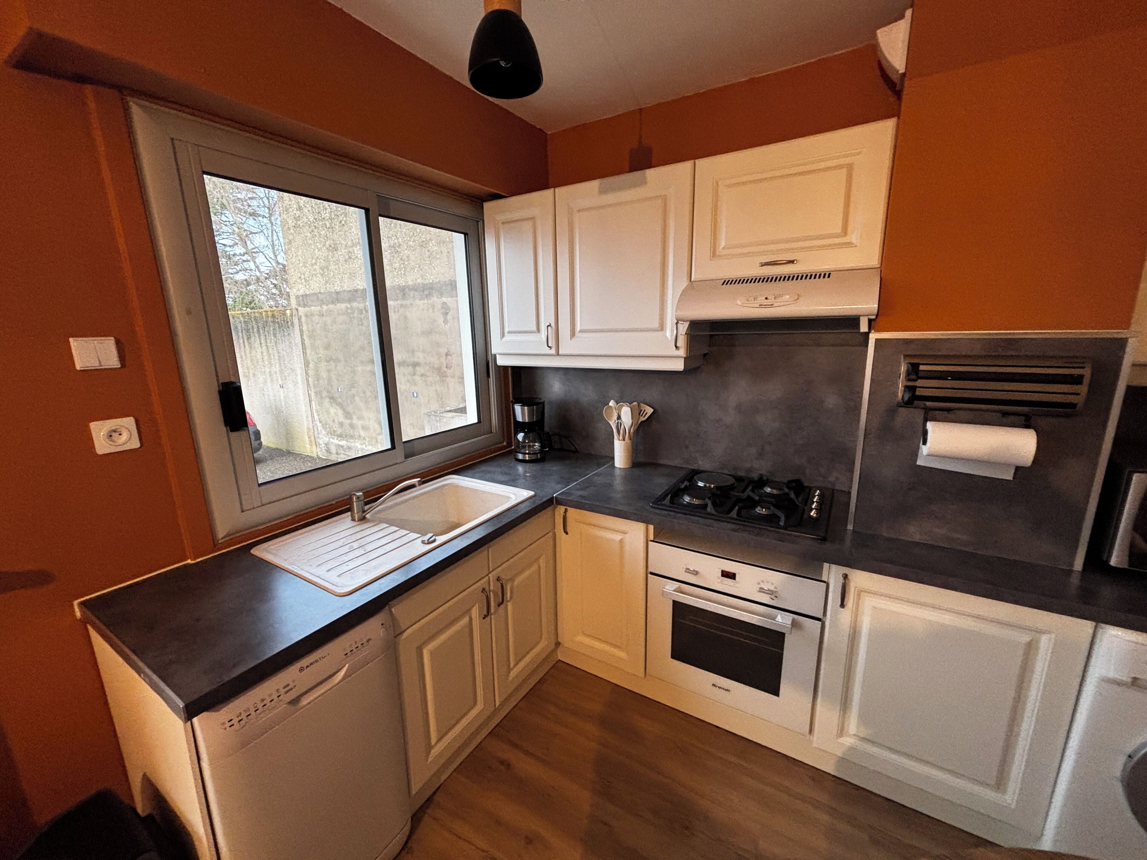 A compact kitchen with white cabinets, a dishwasher, a stove, and a window.