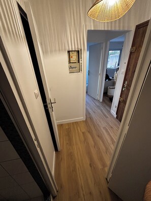 Een gang met houten vloer, witte muren en een deur met lichtschakelaar.