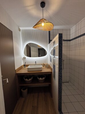 Un baño con tocador de madera, un espejo grande, una lámpara colgante y zona de ducha.