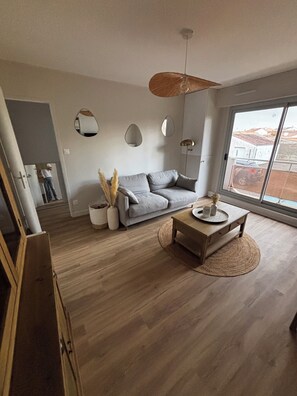 Un salón espacioso con un sofá gris, una mesa de centro de madera y un ventanal con vistas al exterior.