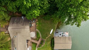 Eine Vogelperspektive auf ein Anwesen mit einer großen Terrasse, einer runden Lounge-Ecke und einem Steg, der ins Seeufer führt.