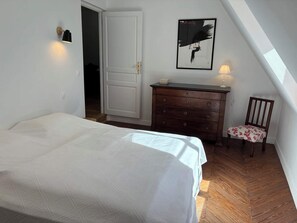 Ein Schlafzimmer mit Bett, Schminktisch, Stuhl, Tür und einer Wandlampe.
