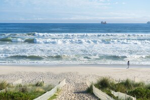 Ein Strand mit einer Person, Wellen und Schiffen in der Ferne.