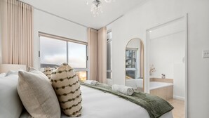 Ett hotellrum med en stor säng, utsikt över havet, ett badrum med badkar och en spegel.