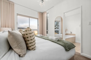 Ein Hotelzimmer mit einem großen Bett, Meerblick, einem Badezimmer mit Badewanne und einem Spiegel.