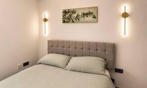 Ein Bett mit einer gebügelten Kopfteil, zwei Nachttischlampen und einem an der Wand hängenden Kunstwerk.