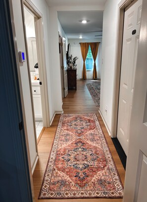 A hallway with a patterned rug, wooden flooring, white walls, and a door on the right. - An Elevated Countryside Escape Just Outside of Collierville  (Byhalia)