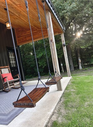 A wooden porch with a swing set, a rocking chair, and a door with a window.