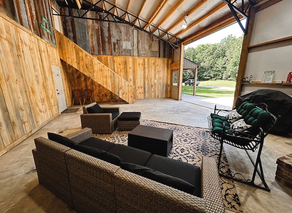 A covered outdoor seating area with wicker furniture, a grill, and a view of the outdoors.