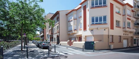 A multi-story residential building with balconies, a gated entrance, and a clear sky.