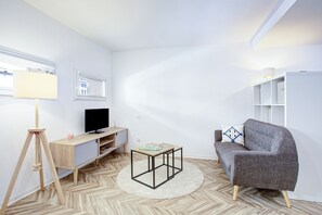 A modern living room with a sofa, a small table, a lamp, a TV, and a bookshelf. - Le Bourdon - Terrasse - Centre-ville (Perpignan)