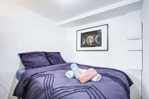 Ein Schlafzimmer mit einem Bett, Kissen, einem gerahmten Bild und einer weißen Wand.