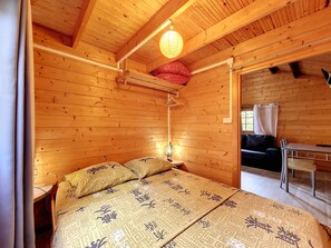 Ein Zimmer in einer Holzhütte mit einem Bett, einer Hängeleuchte und einem Fenster mit Vorhang.