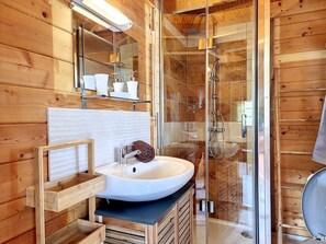 Un baño de cabaña de madera con ducha envuelta en vidrio, un lavabo blanco y un tocador de madera.