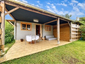Eine Holzhütte mit überdachter Terrasse, einem Tisch mit Stühlen und einem Bett.