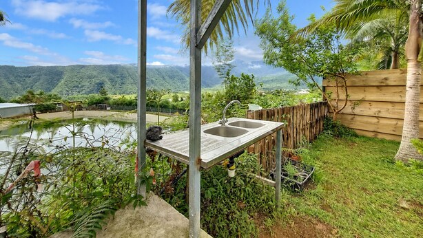 Un espace extérieur abrité doté d’une terrasse en bois, d’un évier en métal et offrant une vue sur un lac et des montagnes.