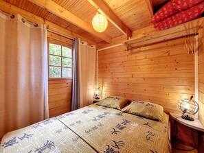 Una habitación de cabaña de madera con cama, cortinas, una ventana y una lámpara fijada a la pared.