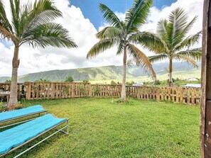 A grassy outdoor area with wooden fencing, a wooden deck, and a view of distant hills. - Le Yucca - Terrasse - TV (Saint-Louis)