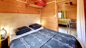 Una stanza in legno con un letto, una lampada a sospensione e vista su un'altra stanza.