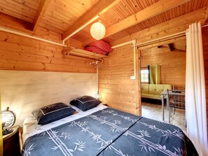 Ein Zimmer in einer Holzhütte mit einem Bett, einer Hängelampe und Blick auf ein weiteres Zimmer.