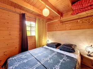 A wooden room with a bed, curtains, a window, and a hanging light fixture. - Le Yucca - Terrasse - TV (Saint-Louis)