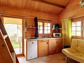 Ein kleines Holzhaus mit einer Küchenzeile, einem kleinen Kühlschrank, einer Mikrowelle und einem Schlafsofa.