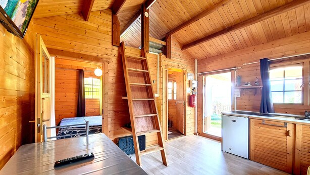 Interno di una baita in legno con cucina, zona pranzo e camera soppalcata.