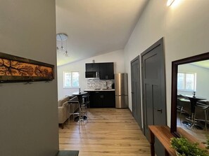 A modern kitchen with dark cabinets, a stainless steel refrigerator, and a dining area with a round table and bar stools. - Spruce Tranquility Studio  (Anchorage)