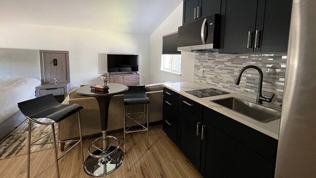 A compact kitchen with black cabinets, a stainless steel sink, and a small dining area with two bar stools.