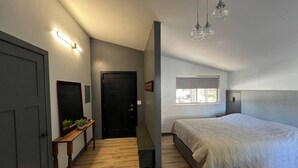 A bedroom with a bed, a bench, a door, and a window.