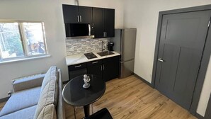 A compact kitchen with black cabinets, a countertop, and a refrigerator. There's a small table with a decorative item.