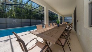 Ett takförsett utomhusområde med plats för måltider, en pool, ett träbord och stolar.