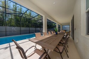 Ein überdachter Essbereich im Freien mit Pool, Holztisch und Stühlen.
