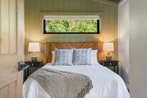 Ein Schlafzimmer mit einem großen Bett, zwei Nachttischen mit Lampen, einem Fenster mit Blick auf Grünflächen und einem Holzkopfstück.