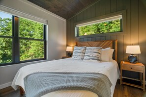 Een slaapkamer met een groot bed, twee nachtkastjes en een raam met uitzicht op bomen.
