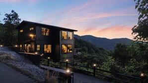 A two-story wooden cabin with multiple windows, a balcony, and a view of a forested mountain range. - Sugar Maple Summit a Luxury Cabin w/ Breathtaking Views in Shagbark (Sevierville)