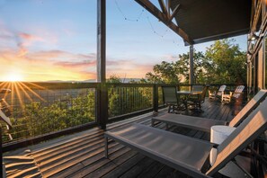 Eine Holzdielen-Terrasse mit Liegestühlen und einem Tisch, mit Blick auf eine malerische Landschaft bei Sonnenuntergang.