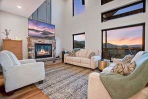 A living room with a fireplace, a sofa, a chair, and a view of the mountains. - Sugar Maple Summit a Luxury Cabin w/ Breathtaking Views in Shagbark (Sevierville)