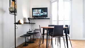Ein modernes Wohnzimmer mit einem Wand-Fernseher, einem Esstisch mit Stühlen, einer Stehlampe und einem Fenster mit Blick.