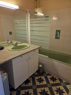 Un baño con lavabo, espejo y bañera verde.