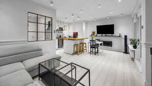 A modern living room with a sofa, glass coffee table, and a kitchen area with a dining table and chairs.