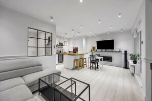 Ein modernes Wohnzimmer mit einer Couch, einem Glastisch und einer Küchenzeile mit Esstisch und Stühlen.