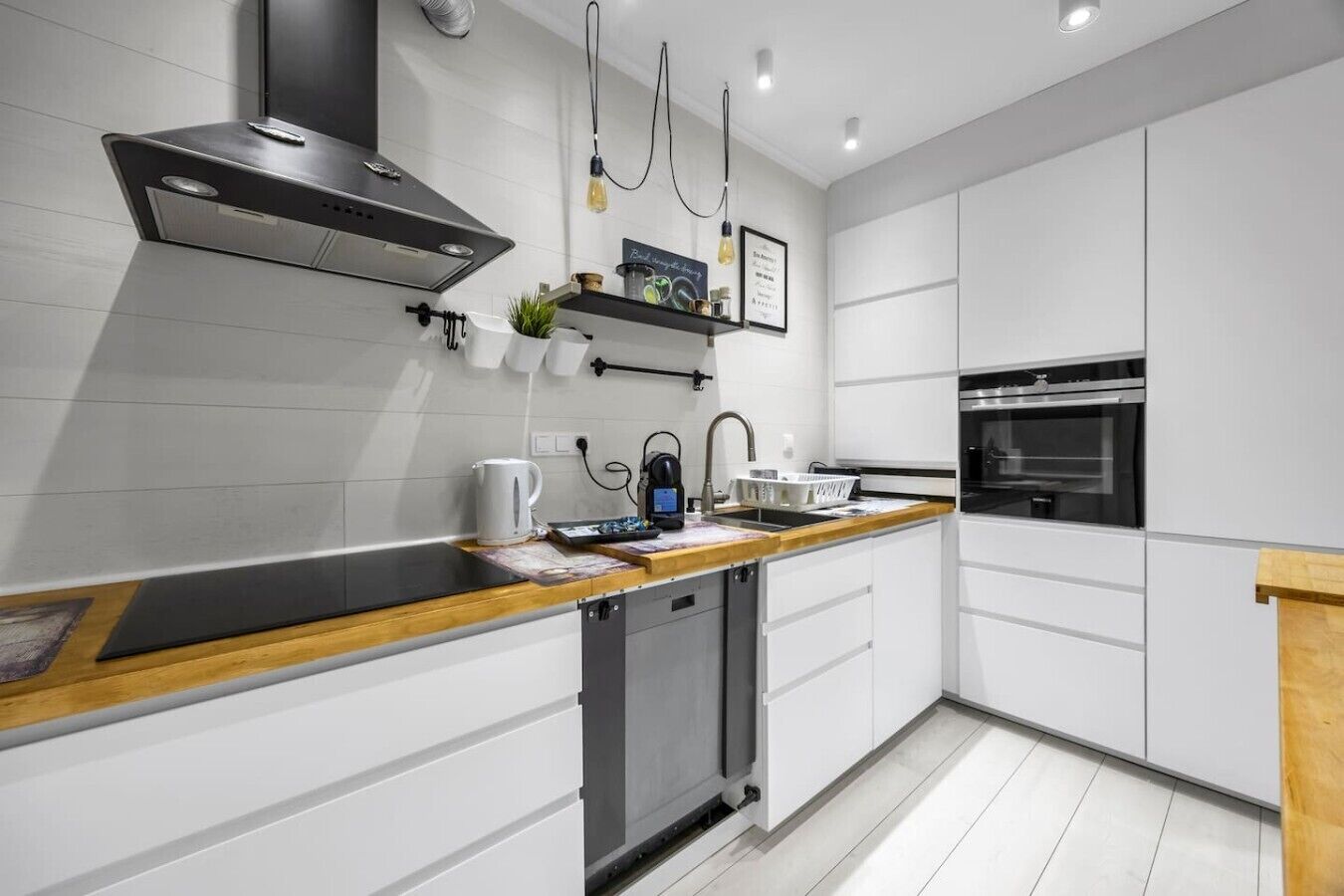 Una cocina moderna con armarios blancos, una campana extractora de acero inoxidable, una encimera de madera y un lavavajillas integrado.