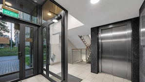 A modern building entrance with glass doors, a sign indicating 'WYJŚCIE,' and a staircase leading to an upper floor.