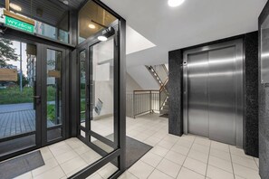 Ein moderner Gebäudeeingang mit Glastüren, einem Schild mit der Aufschrift 'WYJŚCIE' und einer Treppe, die zu einer oberen Etage führt.